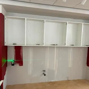 Vita överskåp monterade på väggen, en grön laserlinje syns på väggen under