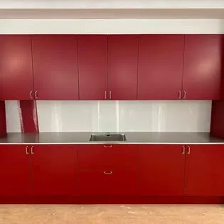 Färdigt kök med röda luckor, rostfri bänkskiva och vitt stänkskydd i glas